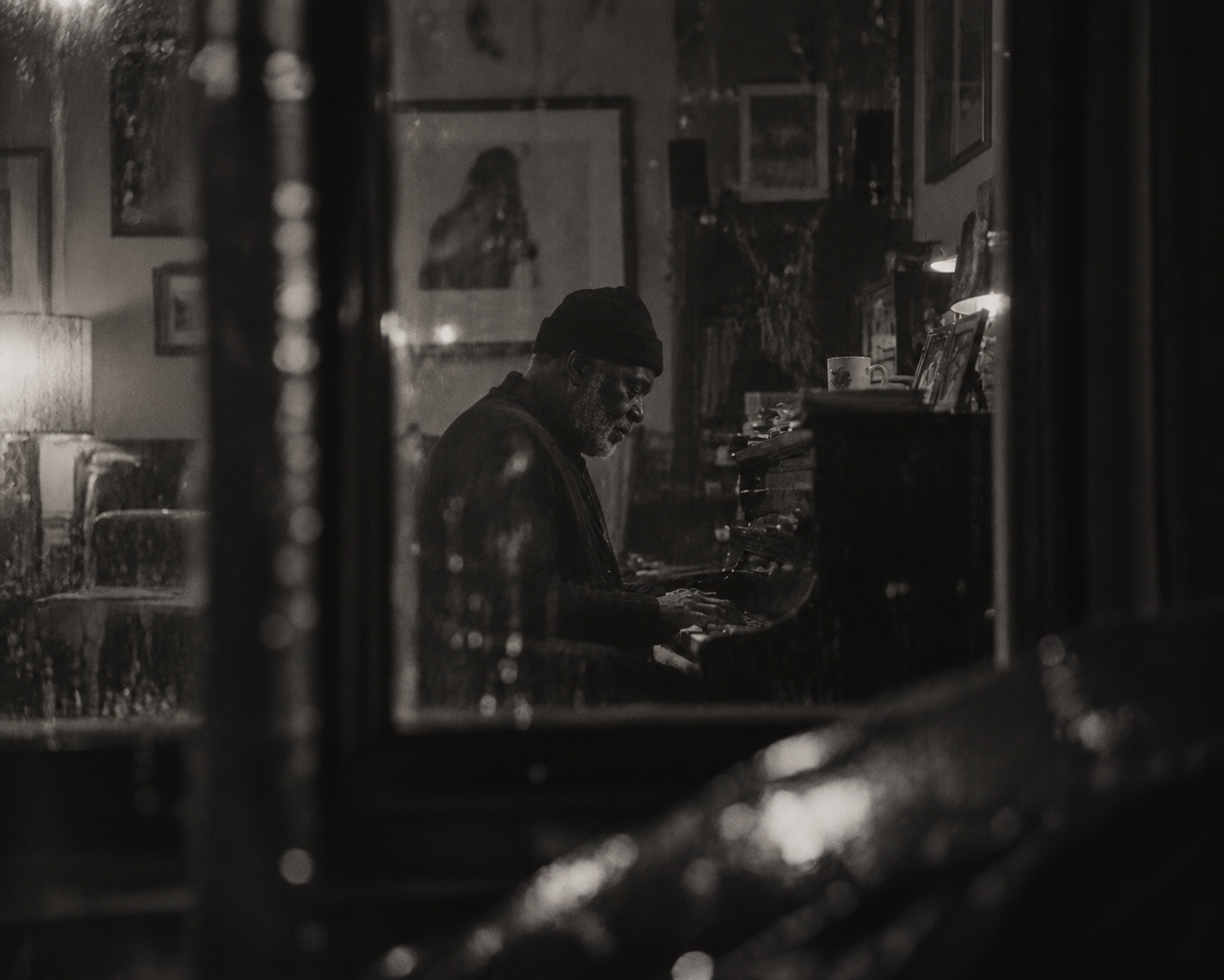 Man playing piano seen through a rain-covered window
