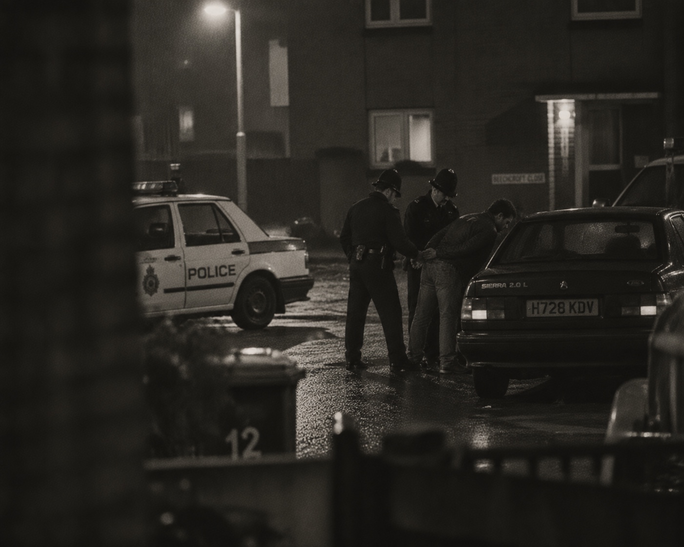 Police arresting a man beside parked cars at night