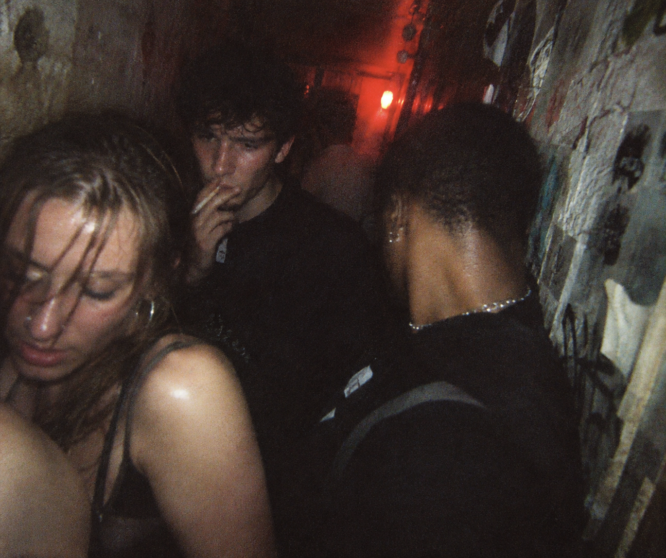 Clubgoers pressed into a narrow wall-side space under red light