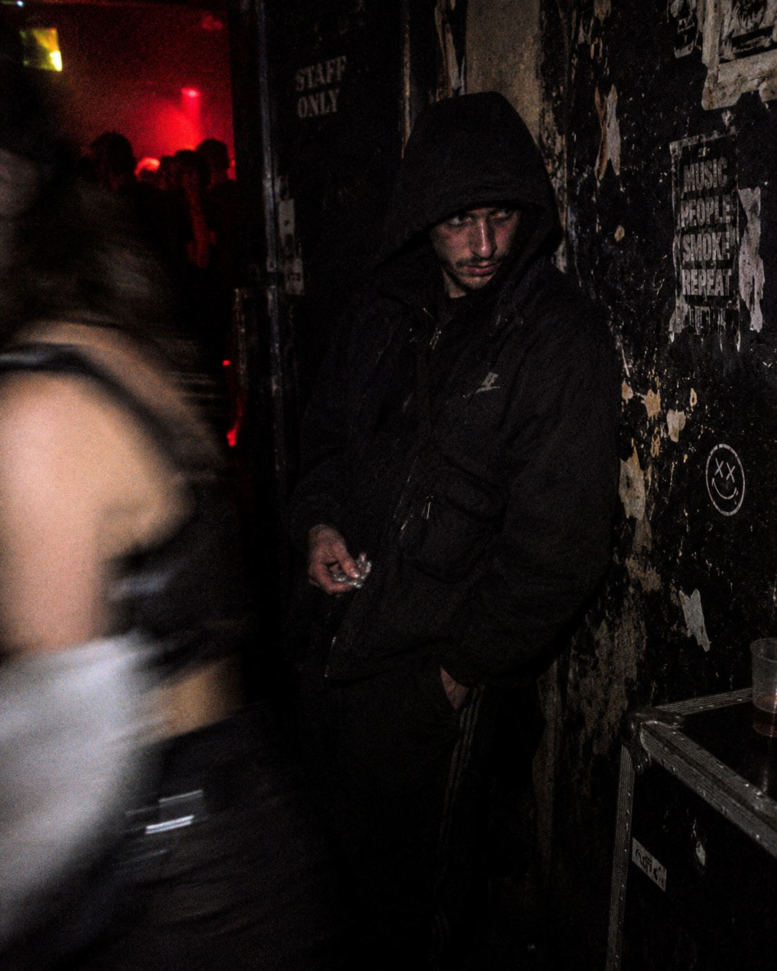 Hooded clubgoer standing against a worn wall