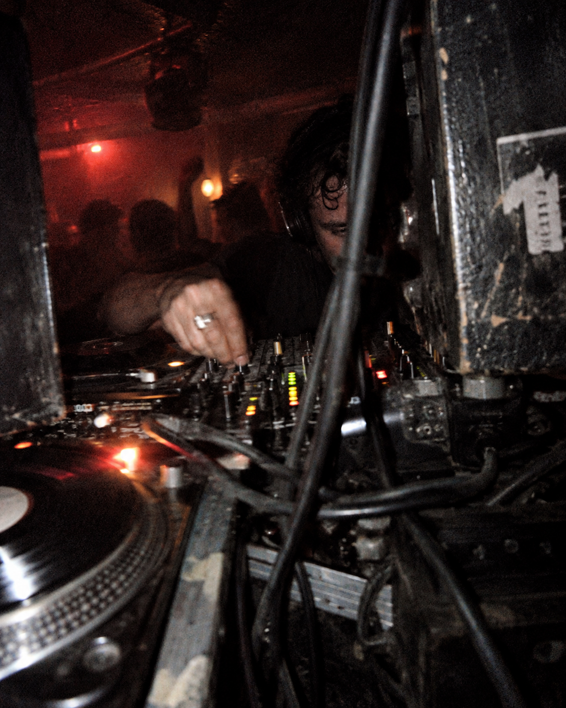 DJ working a mixer behind cables and turntables