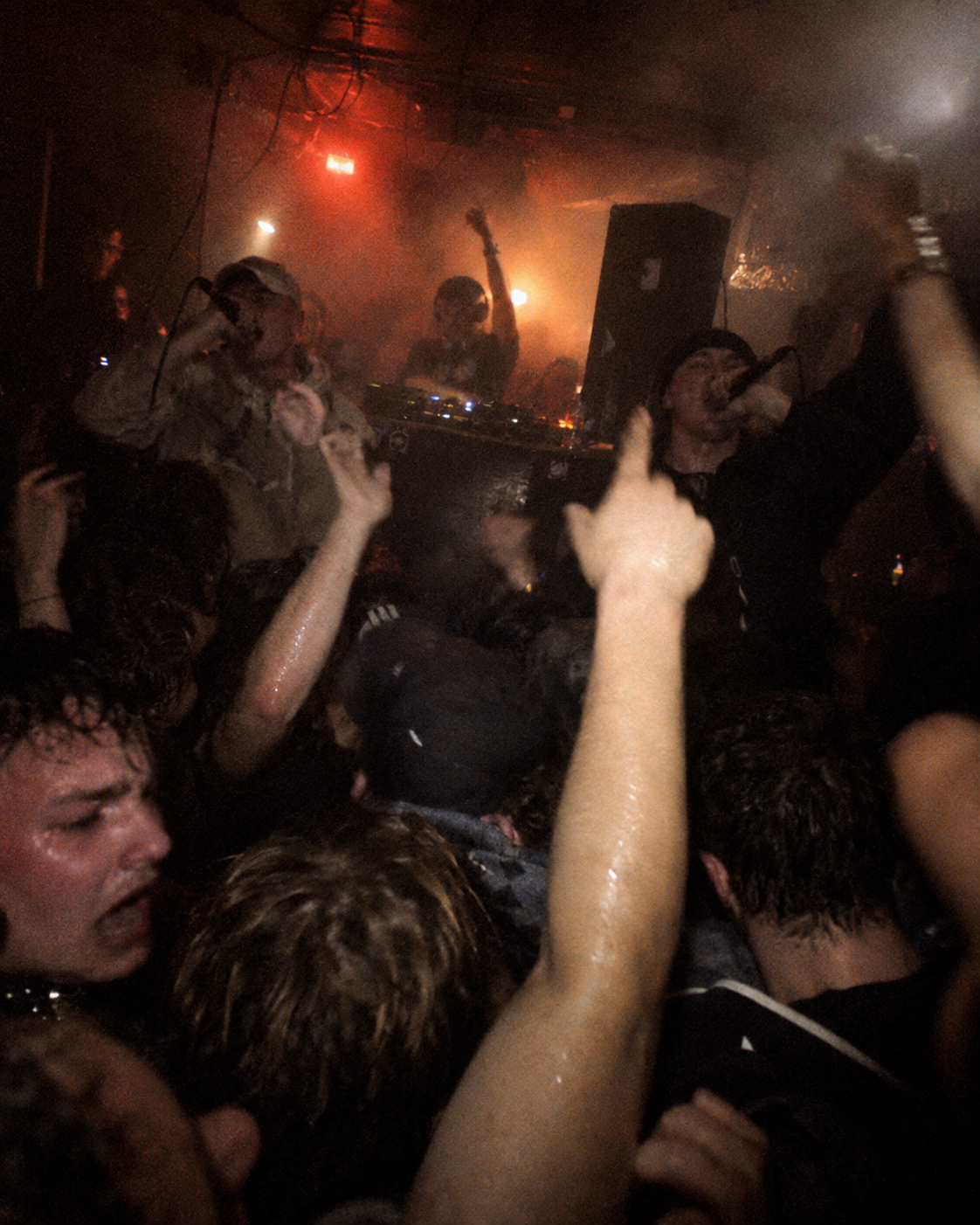 Dense rave crowd facing a DJ under red light
