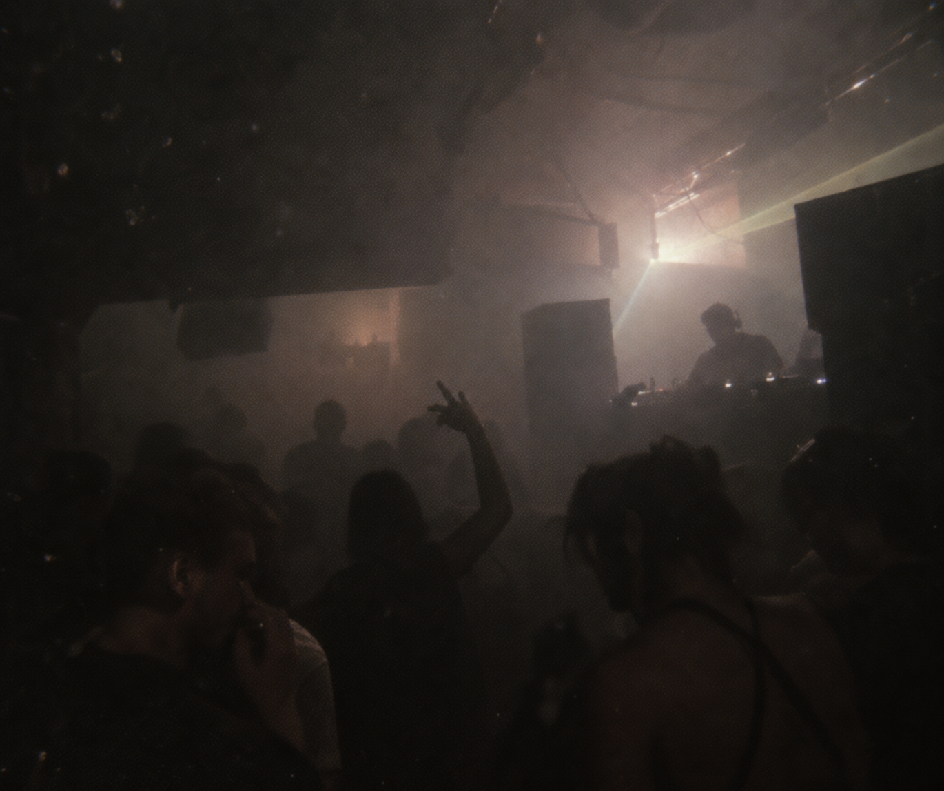 Crowded rave floor facing a DJ through haze and light