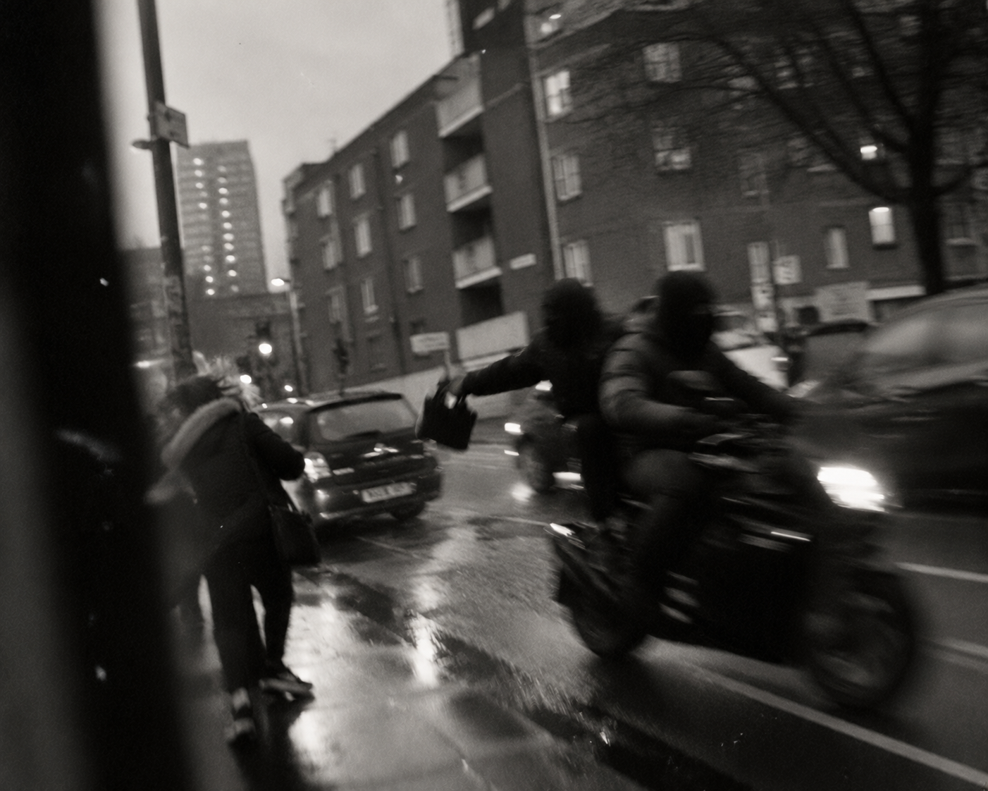 Two masked riders on a scooter moving through wet city traffic