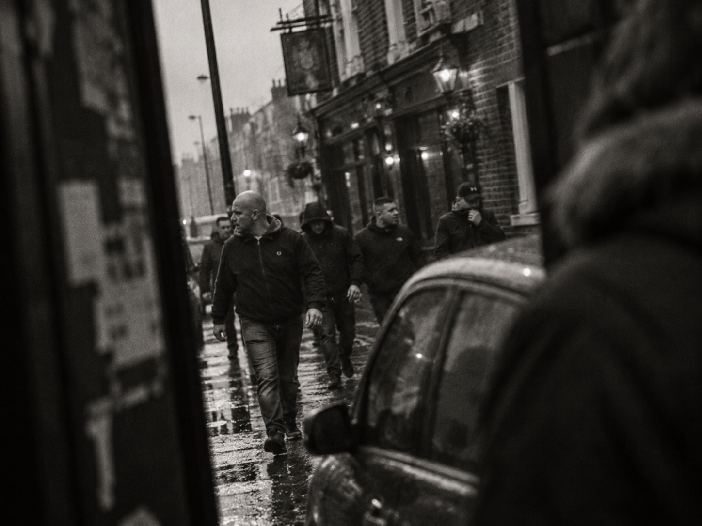 Group of men walking down a wet street outside a pub